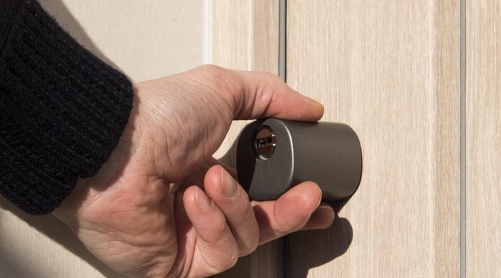Mano che gira il pomolo esterno di un cilindro europeo smart con la chiave inserita, su una porta d'ingresso in legno